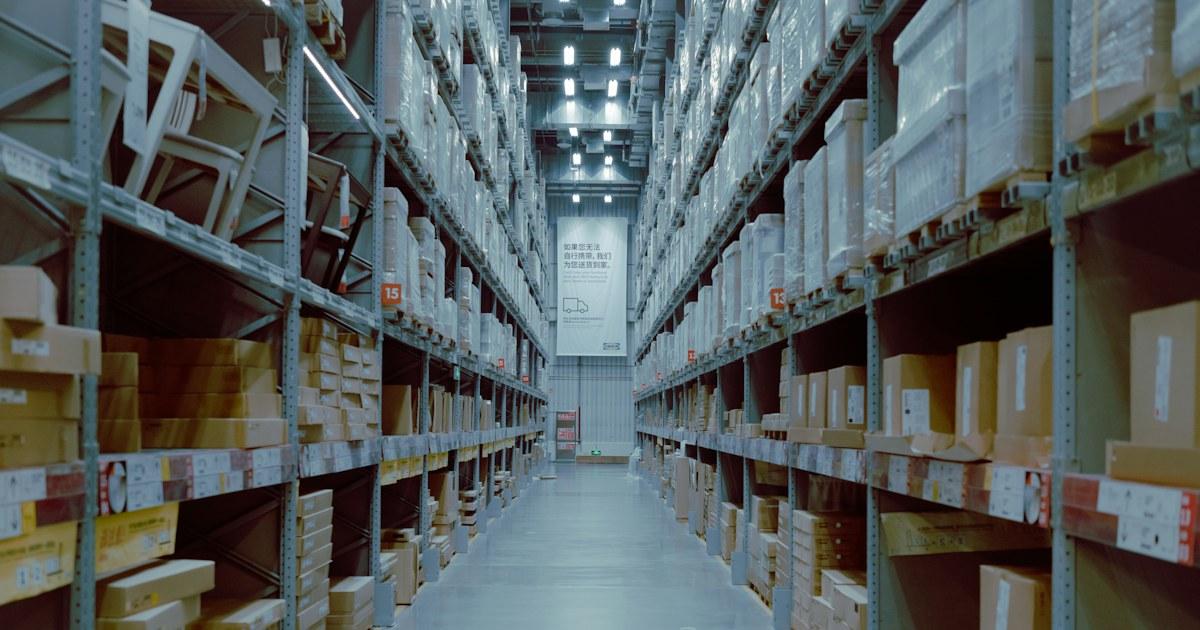 Stocking Kratom Products: What Retailers Check Before They OrderLong warehouse
aisle between tall metal shelving units stacked with cardboard cartons under
overhead lights